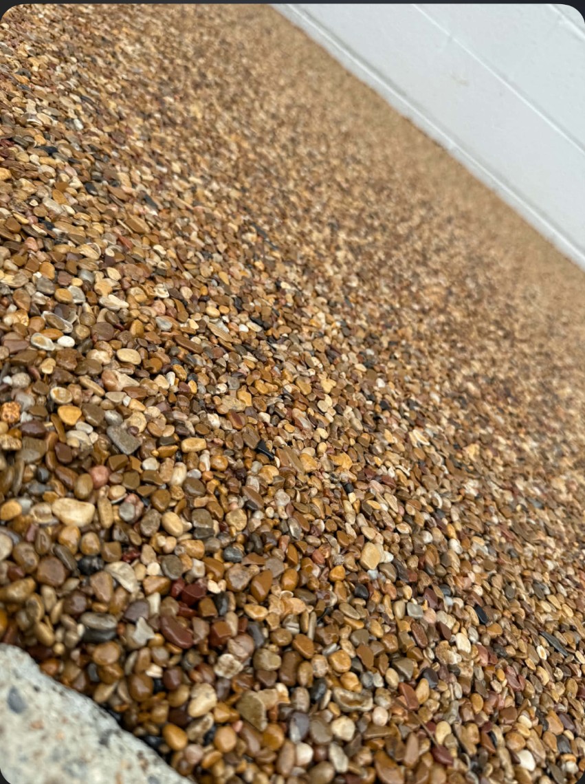 Apache Stone Wrap floor — warm gold and amber pebble blend running up to a white block wall